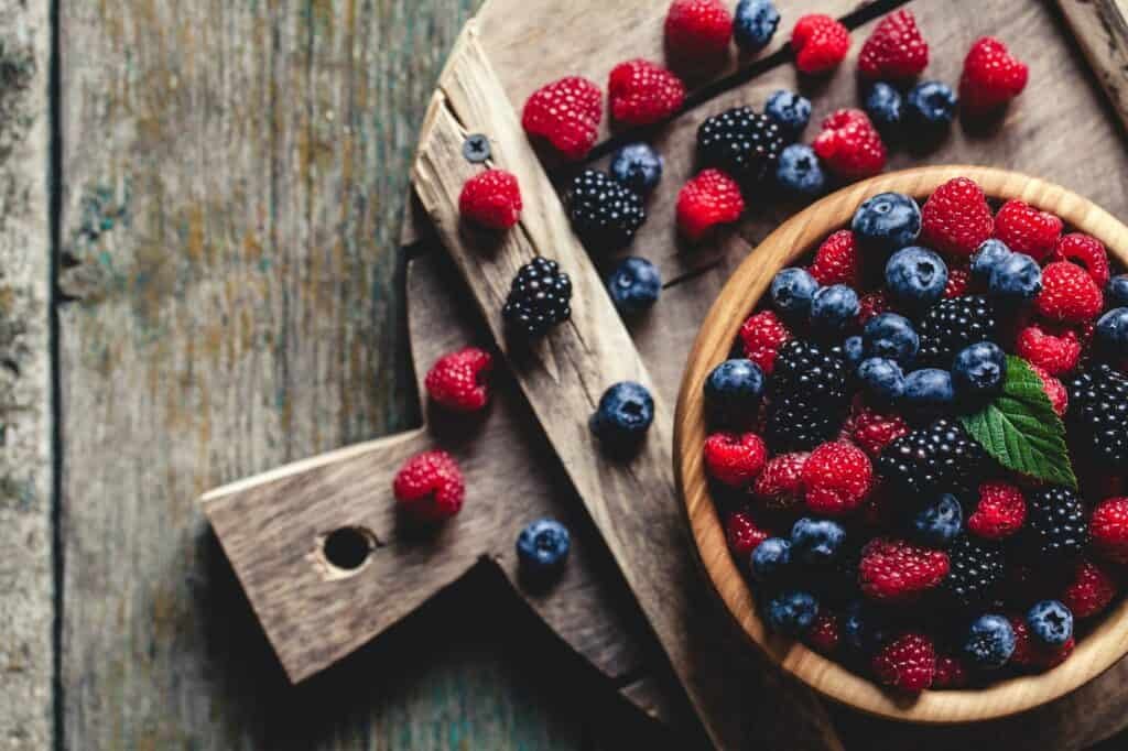 blueberries and raspberries, blackberry in a wooden bowl on old wood background. Perfect for Berry Melomel.