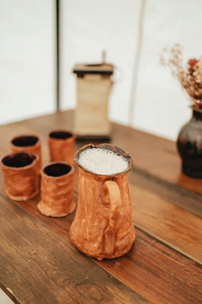 Vertical closeup shot of handmade pottery cups with one full of mead beer on a wooden table