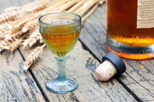 Vintage crystal brandy glass with bottle, cork and rye in the background. Result of 1-gallon mead recipes.