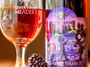 A glass of mead and a bottle of Blackberry Parade melomel from Silver Hand Meadery