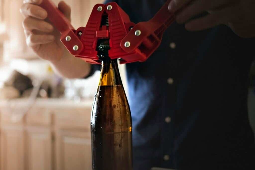 Close up of man using crown corker for closing bottle top of home brew mead